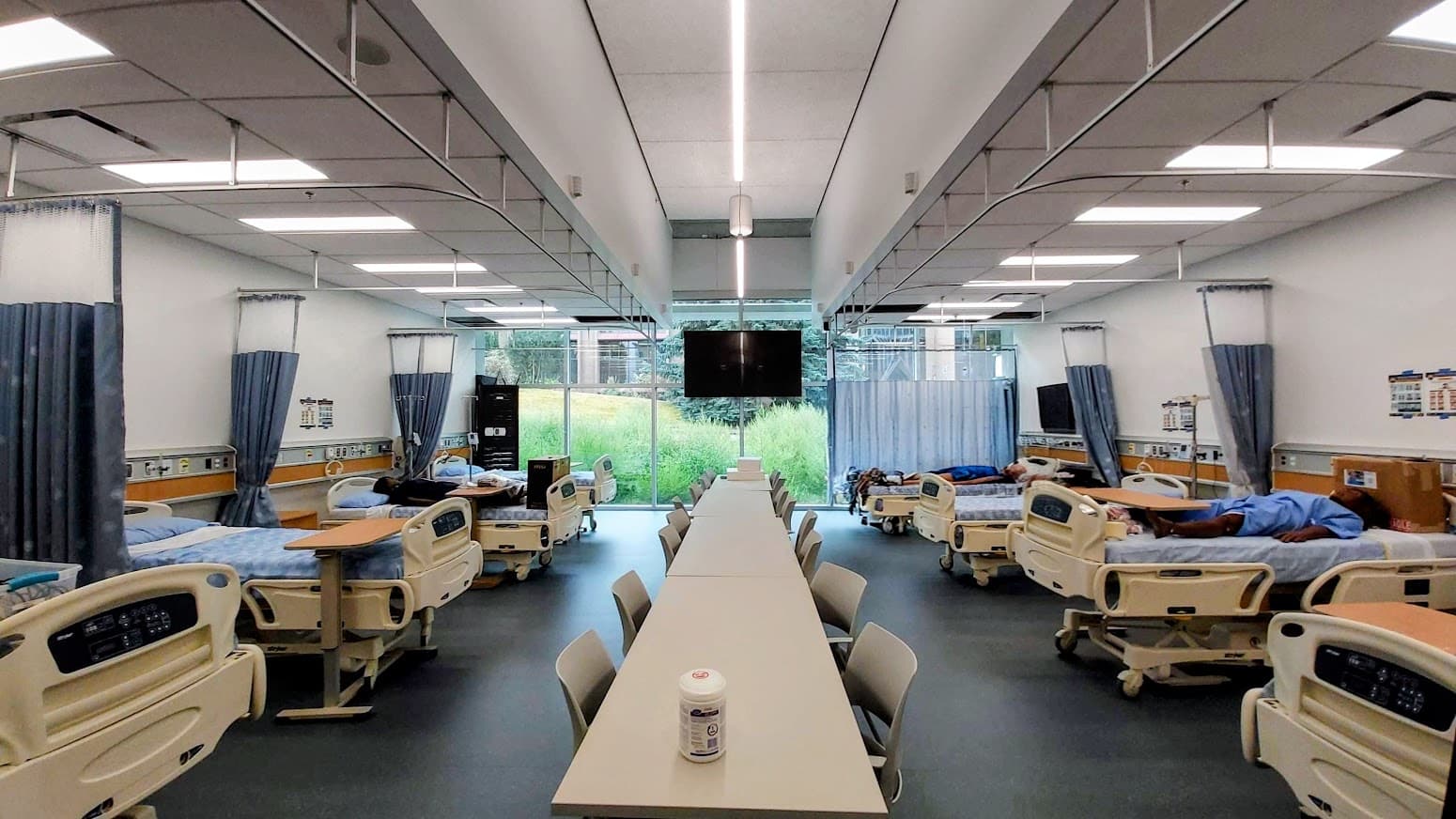 Thompson Rivers University nursing simulation lab with clinical beds arranged around a central learning table.
